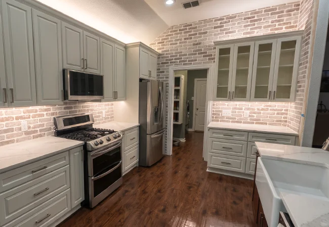 Renovated kitchen with sage green cabinets, whitewashed brick accent wall and stainless steel appliances
